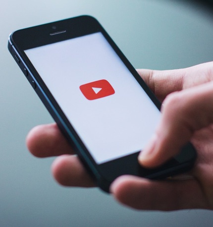 A hand holding a smartphone displaying the YouTube logo, ready to watch videos on acoustic insulation techniques to enhance sound comfort.